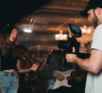 Man Taking a Video of a Woman Carrying a Violin